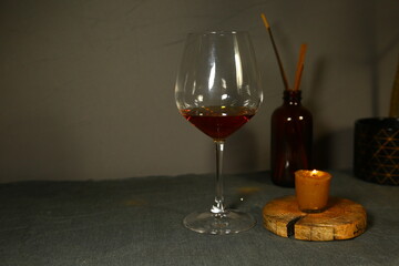 Glass of gold brandy and burning wax candle on candlestick on holiday decor background with empty copy space. Closeup drink celebration ornament