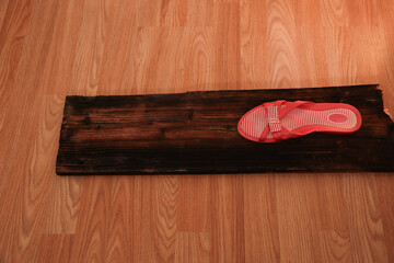 Red flip-flop on weathered wooden plank against blonde hardwood floor
