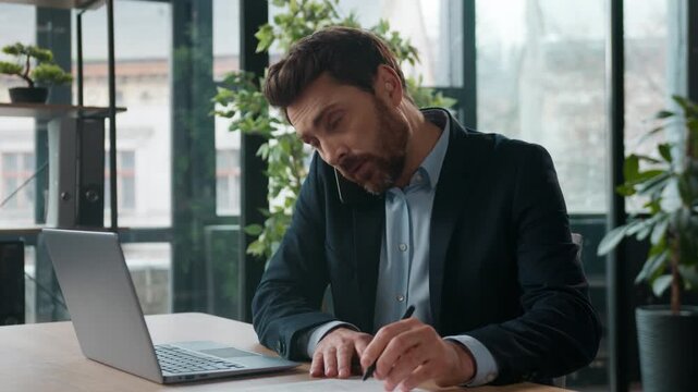 Multitasking Caucasian businessman discuss mobile phone typing laptop in office frustrated male manager business man displeased guy consultant entrepreneur checking information arguing client indoors