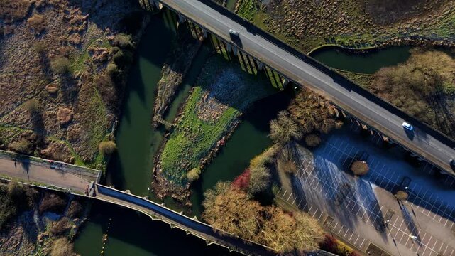 Top down aerial view of vehicles cars and traffic crossing archway bridge over the River Nene near Wellingborough, United Kingdom. Winter bright sunlight. Transport and logistics commuting