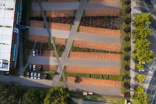 Aerial view of a parking lot with terracotta-colored sections and linear patches of greenery, blending urban design with natural elements, Dresden, Saxony, Germany.