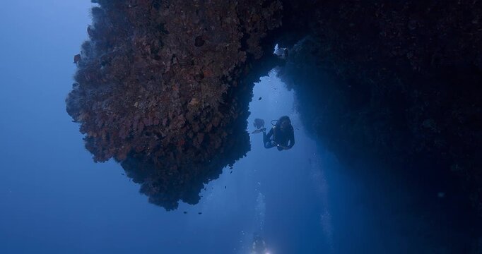 Scuba diver explores overhang on deep coral reef.