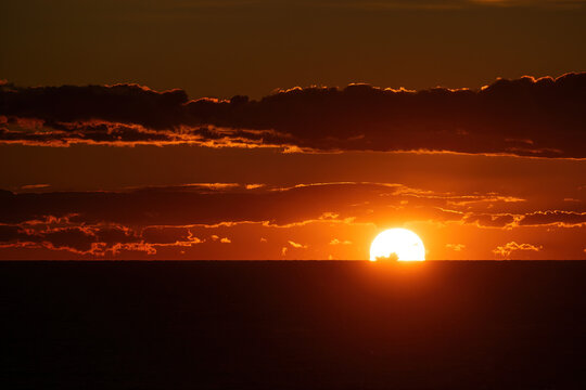 Aerial view of the sun dips below the horizon, painting the sky with fiery hues above the dark sea, Alicante, Valencian Community, Spain.