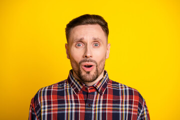 Obraz premium Surprised young man in plaid shirt stands against a bright yellow background for lifestyle fashion or advertising visuals
