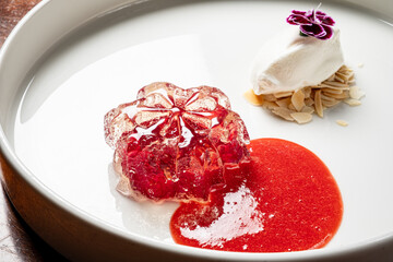 A beautifully crafted dessert features a floral jelly alongside almond cream and berry sauce