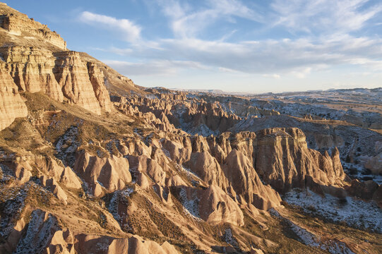 Aerial view of the rugged, sun-kissed landscape, where the soft glow paints the fairy chimneys and rocky formations in warm hues, Cappadocia, Turkey.