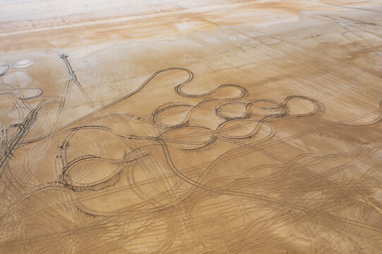 Aerial view of tire tracks etched across the vast, sun-baked expanse of Lake Tuz, creating swirling patterns in the beige landscape, Lake Tuz, saray/van, Turkey.
