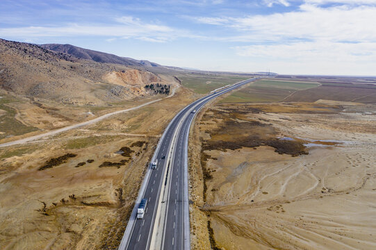 Aerial view of a long straight highway cutting through the arid landscape, contrasting with the distant mountains, Lake Tuz, saray/van, Turkey.