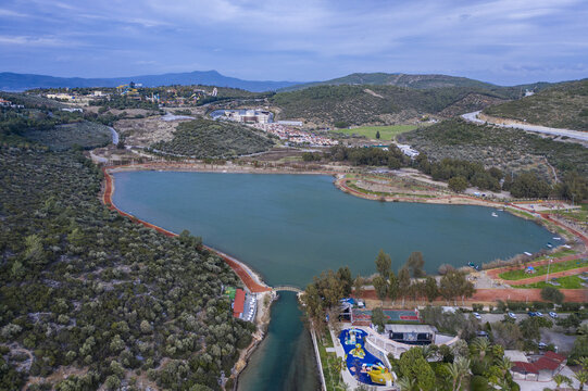 Aerial view of a tranquil lake mirroring the sky, nestled amidst rolling hills and lush greenery, near a water park, Kusadasi, Aydin, Turkey.