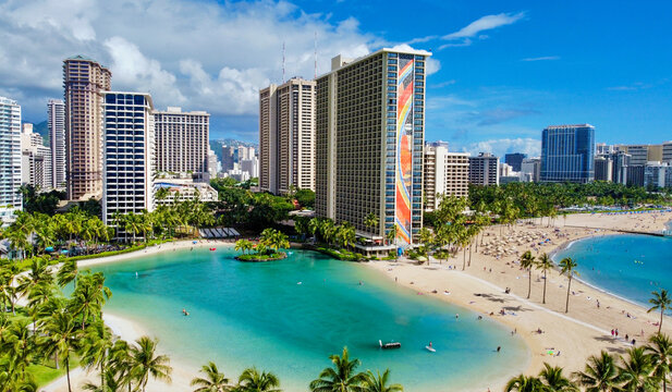 Aerial view of the Hilton Lagoon's turquoise waters contrasting with the golden sands and towering buildings under a vibrant sky, Honolulu, Hawaii, United States.