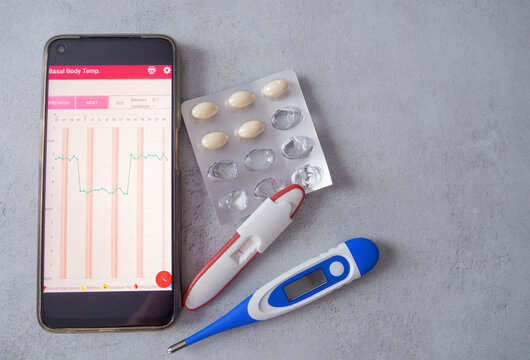Fertility tracking tools, including a BBT thermometer, an app displaying a temperature chart, and supplements for pregnancy planning. A modern approach to women's reproductive health.