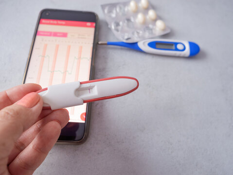 planning a pregnancy, woman is tracking her fertility by measuring her basal body temperature (BBT) with a digital thermometer and logging the data on a smartphone app.