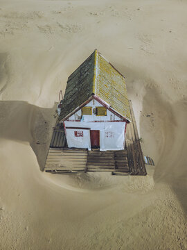 Aerial view of a weathered beach house standing solitary amidst the vast expanse of golden sands, a testament to resilience against the elements, Costa da Caparica, Setubal, Portugal.