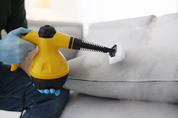 Pest control worker cleaning cushion with steam cleaner indoors, closeup