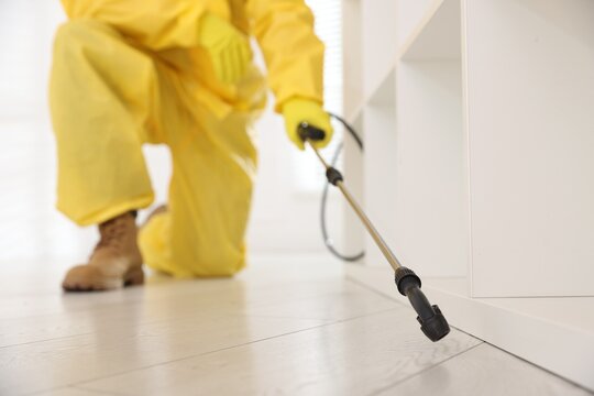 Pest control worker in protective suit spraying insecticide indoors, closeup