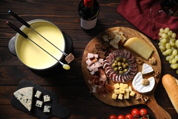 Delicious melted cheese in fondue pot, snacks and bottle of wine on wooden table, flat lay
