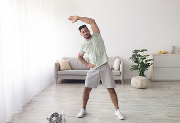 Sporty young Arab man exercising at home during coronavirus lockdown, full length portrait....