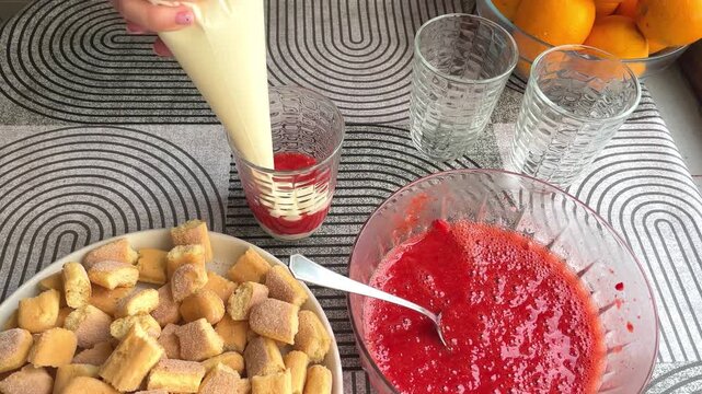 Hand piping cream for strawberry tiramisu in glass. 4K horizontal recipe footage shows a female hand layering a smooth dessert using a pastry bag during sweet preparation.