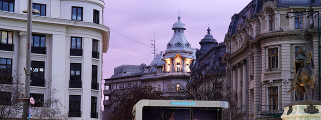 View in the University Square in Bucharest at dusk, with historical buildings, statue and cover of bus stop shelter