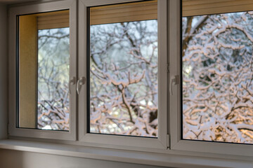 A window frame in a comfortable room shows snow-covered trees outside during winter