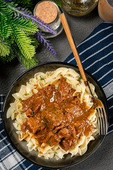 Pasta with beef stew in black bowl.