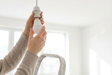 Person replaces light bulb in a bright room while standing on a ladder during the day to improve lighting in the home space