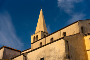 Porec, Croatia - August 13, 2025: A tall church steeple rises against a deep blue sky, its warm sunlit walls and arched windows creating a striking contrast and serene architectural view.