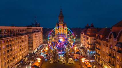 Aerial view of Christmas lights twinkle on the Ferris wheel, casting a festive glow over Victory Square and Metropolitan Cathedral, Timisoara, Timis, Romania.