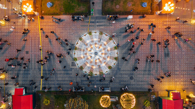 Aerial view of festive lights casting a warm glow over the bustling square, illuminating the patterned pavement and the gathering crowd, Timisoara, Timis, Romania.