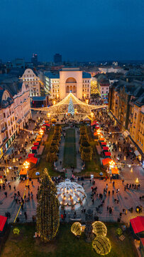 Aerial view of a vibrant, illuminated fair leading to a grand archway, casting a warm glow over bustling crowds and festive stalls, Timisoara, Timis, Romania.