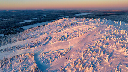 Aerial view of snow-laden ski tracks cut through frosted forests under a tranquil dawn sky, Salla, Finland.