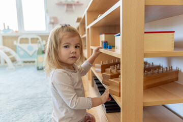Little girl playing alone in the kindergarten with wooden toys