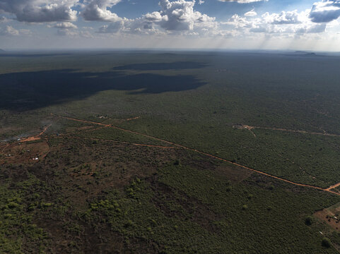 Aerial view of sun-drenched plains meeting shadowed swathes under a vibrant sky, the landscape a mosaic of green and brown, Voi, Taita-Taveta County, Kenya.