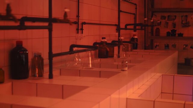 A large old-fashioned industrial photo lab with baths for developing and fixing the image on photographic paper, with chemicals and other photographic equipment and, of course, red light everywhere. S