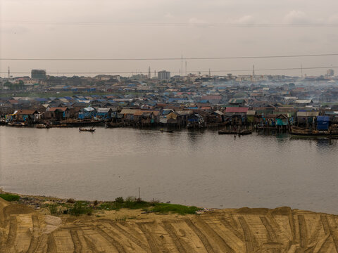 Aerial view of water settlements, with wooden stilt houses reflecting on the water's surface under a hazy sky, Yaba, Lagos, Nigeria.