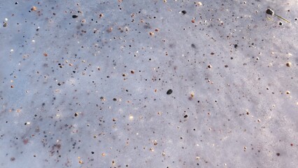 Granite chips on frozen sea water.  A frozen ground surface is speckled with various small pebbles. The icy texture creates a cool, wintry atmosphere.