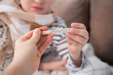 Child with scarf holding thermometer, measuring temperature, cozy indoor setting.
