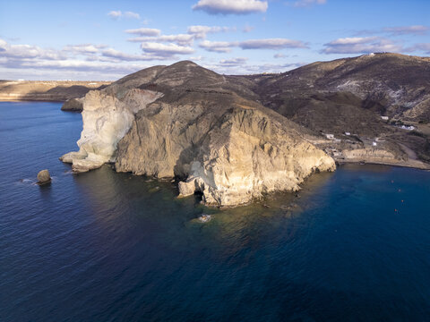 Aerial view of dramatic cliffs plunging into the turquoise sea, where the white rock faces contrast with the dark shadows and deep blue water, White Beach, Santorini, Greece.