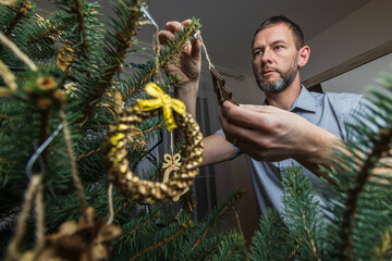 Man in shirt hanging decoration on Christmas tree. Preparing for holidays, Christmas Eve. Lifestyle background