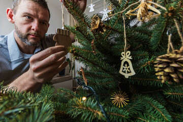 Man in shirt hanging decoration on Christmas tree. Preparing for holidays, Christmas Eve. Lifestyle background