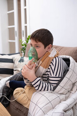 Boy wrapped in blanket using inhaler mask, sitting on sofa at home, recovering from illness, glass of water nearby, cozy indoor setting.