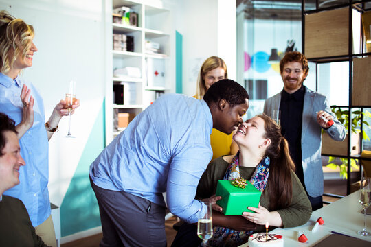 Adult coworkers sharing affectionate birthday moment in modern office