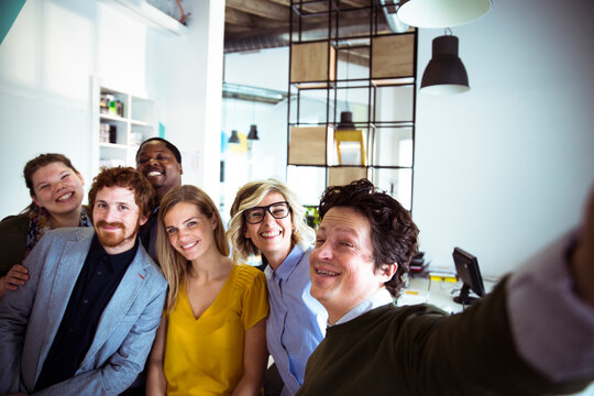 Happy young adults taking a team selfie in modern office