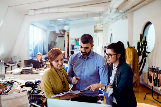 Adult coworkers discussing fashion project in bright creative studio, focused