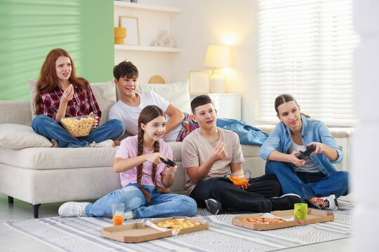 Group of teenagers playing video game and having snacks at home - Powered by Adobe
