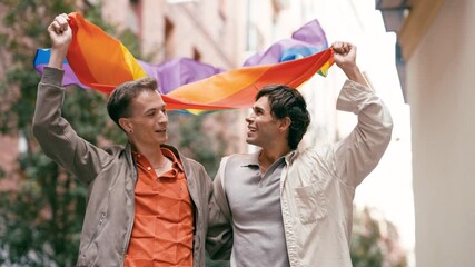 Smiling young gay couple celebrating pride together. Two happy men holding a rainbow flag, symbolizing love, freedom, and equality