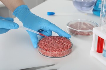 Scientist dripping sample onto raw minced cultured meat at table in laboratory, closeup