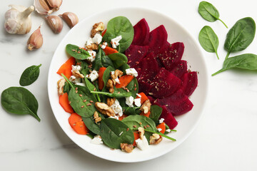 Delicious salad with beetroot, spinach, cheese, walnuts and carrot on white table, top view