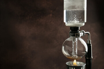 Siphon (vacuum) coffeemaker with hot water against brown background, closeup. Space for text