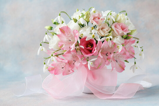 Spring delicate pink and white bouquet with lisianthus, eustoma, alstroemeria, snowdrops and a ribbon bow on a colorful background. Beautiful card